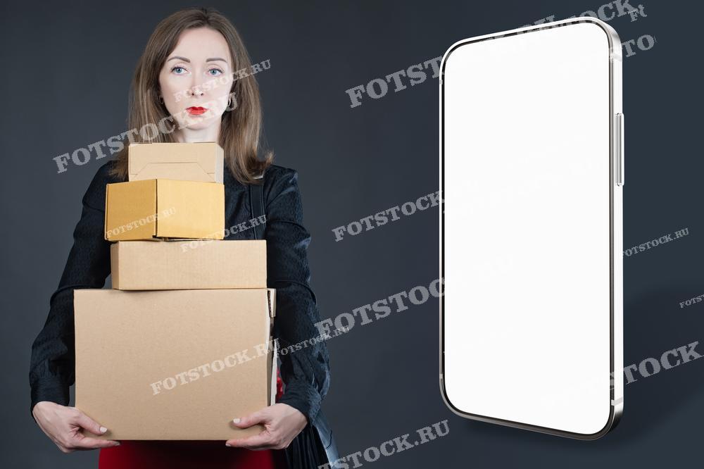 На изображении показана женщина, держащая несколько коробок, рядом с большим смартфоном на сером фоне. Это символизирует использование мобильного приложения для управления процессом хранения и аренды складских ячеек. Современные технологии облегчают подготовку и организацию временного хранения вещей.